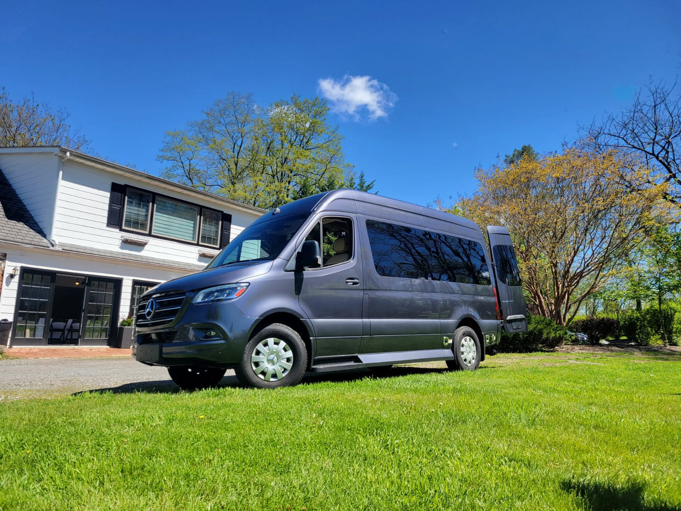 A gray Mercedes Sprinter RV rental is parked on a green lawn by a white house, ready for travel.