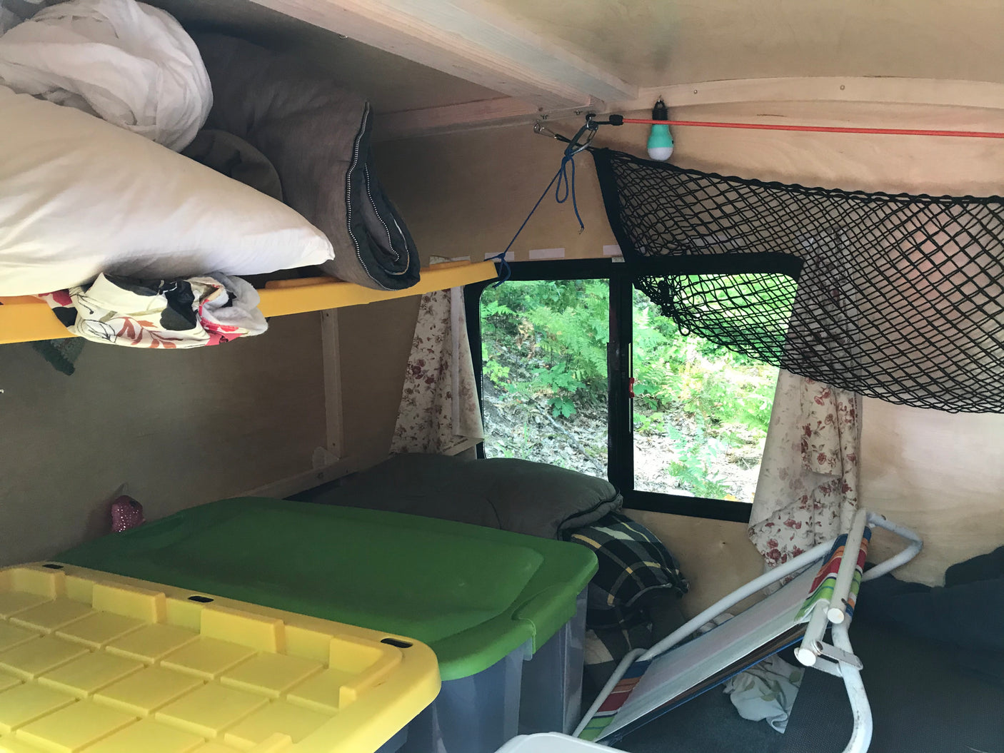 Cozy RV rental interior: bunk bed, storage, and window with lush nature view. Perfect for camping or travel.