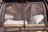 RV rental: Camper van interior with a mesh screen door, revealing a cozy bed and outdoor view through a window.