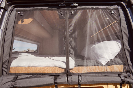 RV rental: Camper van interior with a mesh screen door, revealing a cozy bed and outdoor view through a window.