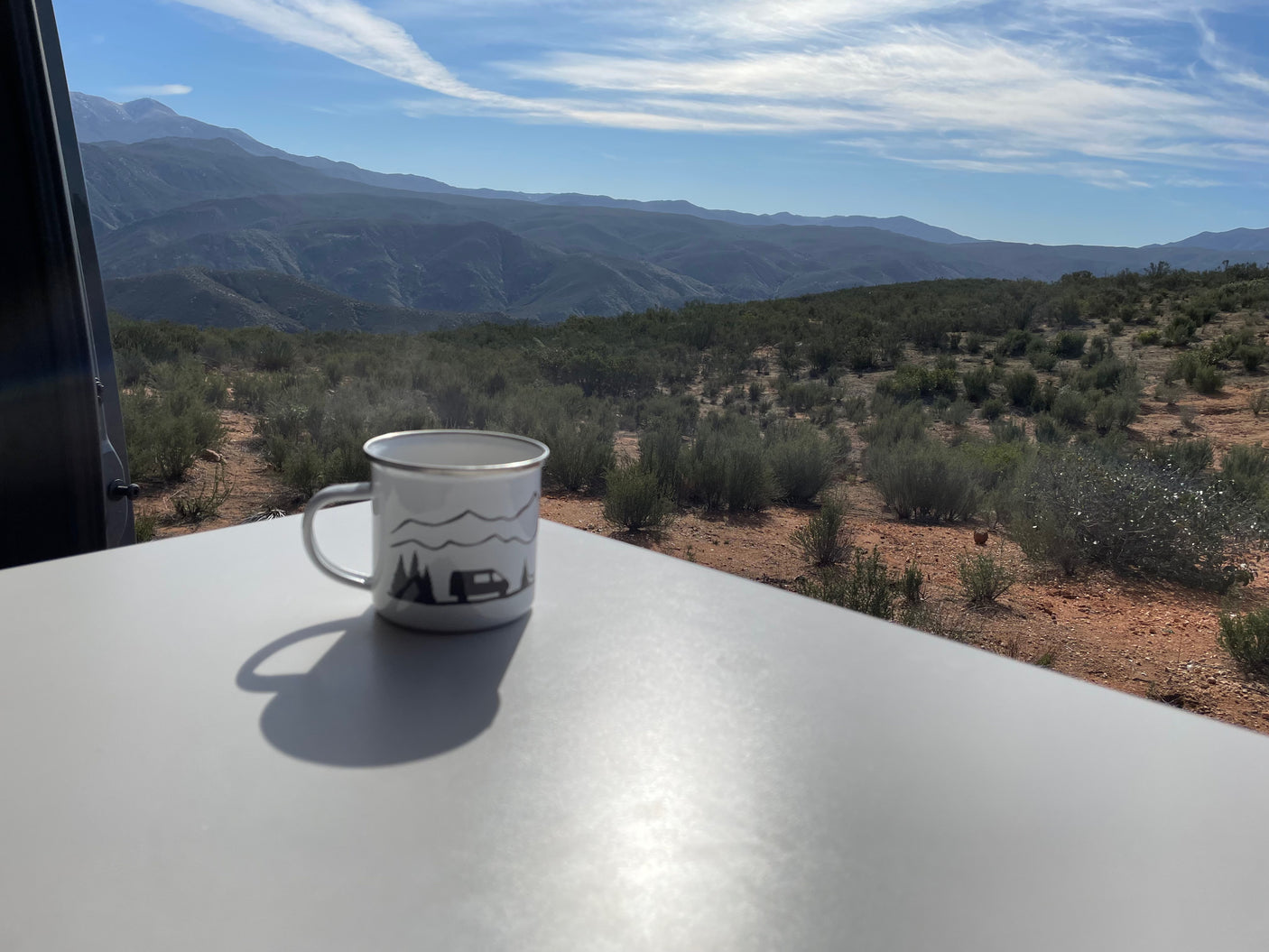 Cozy RV rental view: Steaming coffee mug with scenic mountain and desert landscape.