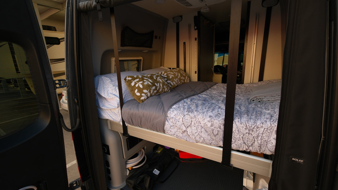 Inside a comfortable RV rental, featuring a made-up bed and storage, seen through the open rear doors.