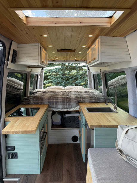 Spacious RV rental camper van interior with a cozy bed, full kitchenette, wooden ceiling, and skylight for an adventurous trip.