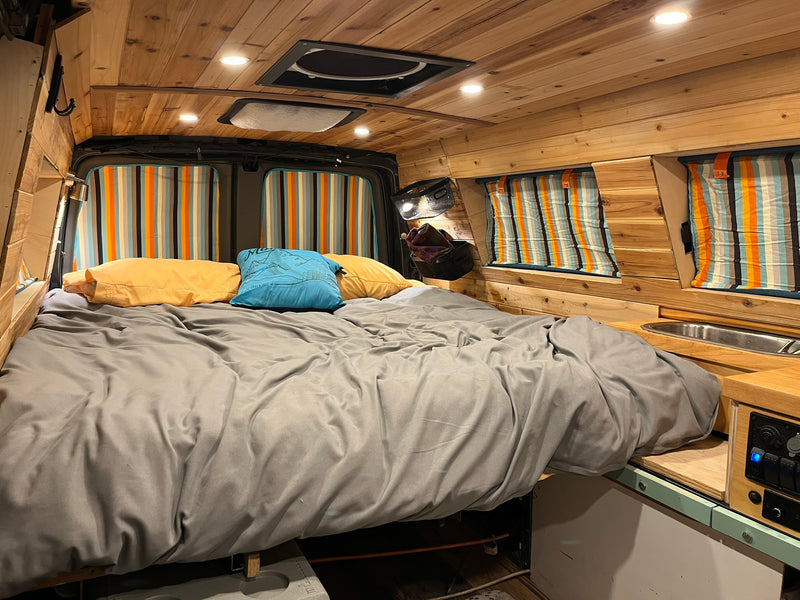 Cozy wood-paneled camper van interior for RV rental. Features a comfortable bed, kitchenette, and bright lighting. — photo 6