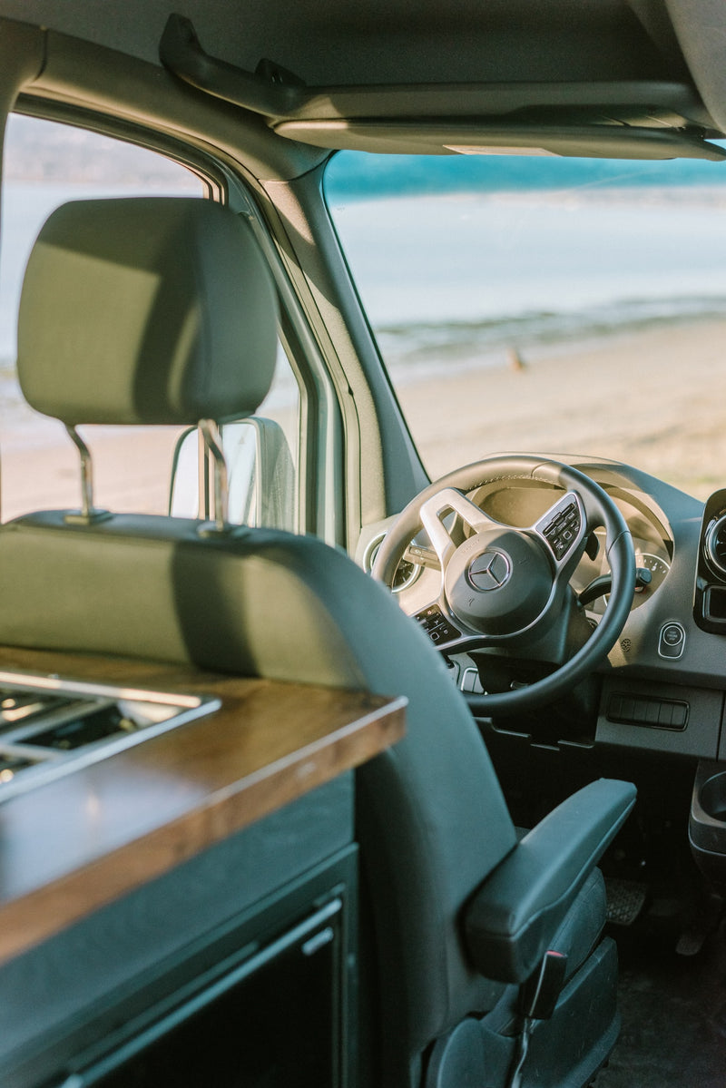 Inside an RV rental: a Mercedes-Benz camper van interior with a steering wheel, parked at a sandy beach. — photo 25