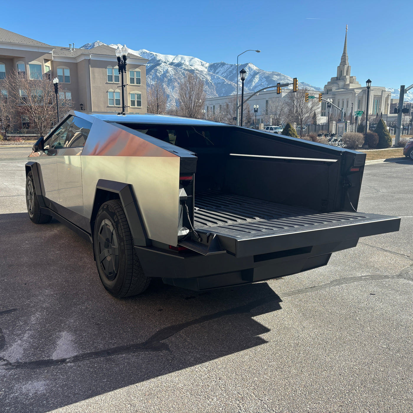A unique Tesla Cybertruck with its tailgate open, hinting at versatile utility. Set against mountains & a temple, it challenges typical rv rental concepts. — photo 6