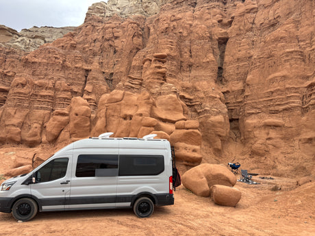 White RV rental camper van parked at a unique desert campsite amidst stunning red rock formations.