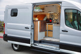 RV rental: A white converted camper van with its side door open, revealing a cozy interior with bed, storage, and lights.