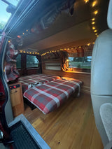 Step inside this cozy RV rental with custom wood accents, comfy plaid beds, and warm string lights.