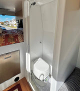 RV rental interior features a compact bed, refrigerator, and wet bath with shower & portable toilet.