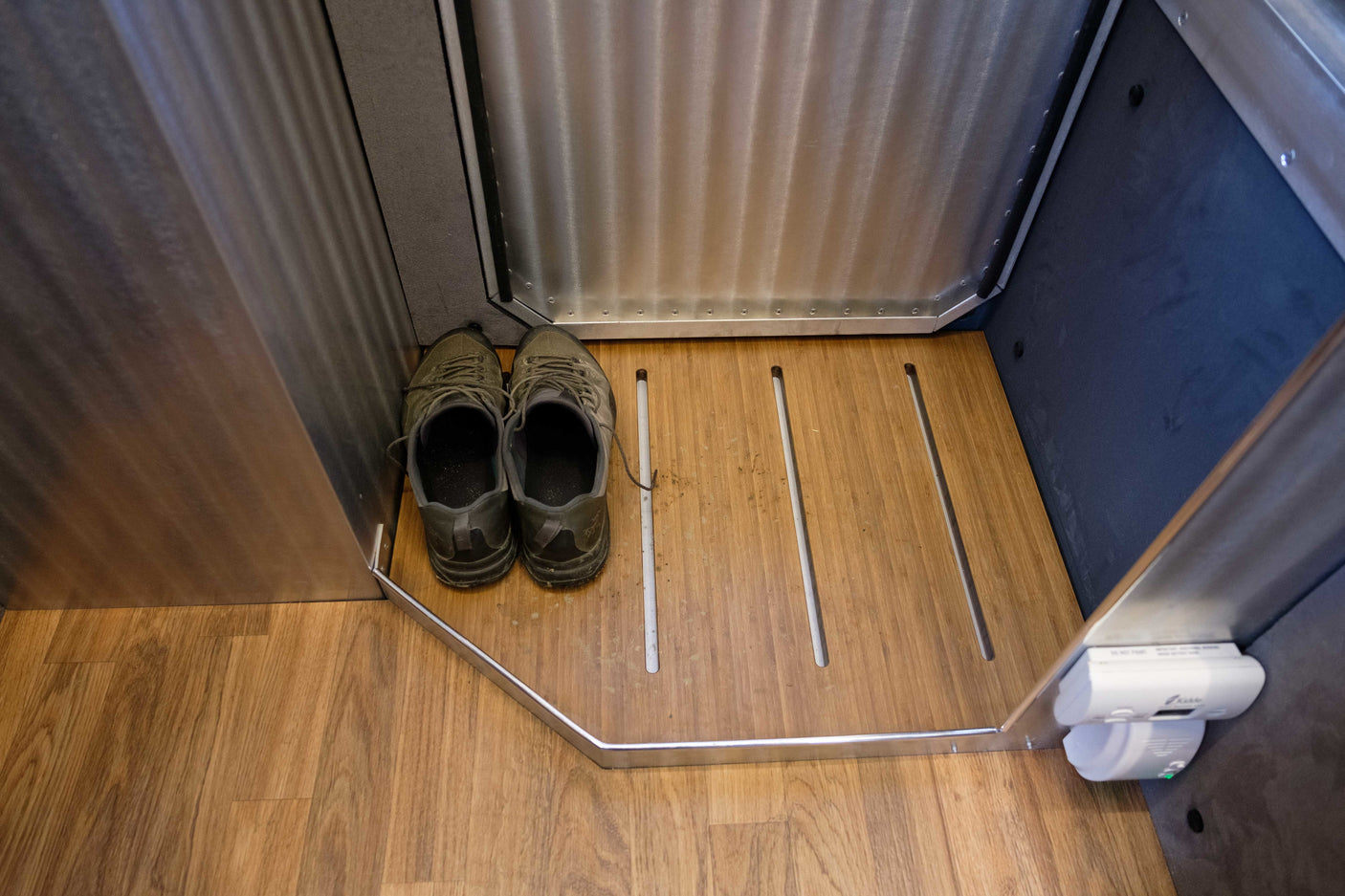 RV rental interior: Shoes on a wooden entry floor with a built-in drying area and safety detector.