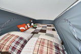 Cozy RV rental pop-top sleeping area with a patchwork bed, stuffed animals, and camping accessories.