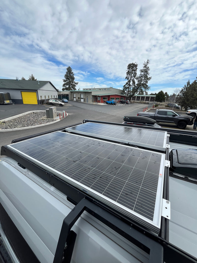 Two large solar panels on an RV rental van rooftop, with commercial buildings & parked cars in the background under cloudy skies. — photo 6