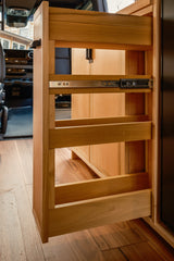RV rental: A light wood pull-out pantry, open to reveal its slatted shelves and metal slide mechanism inside a camper van.