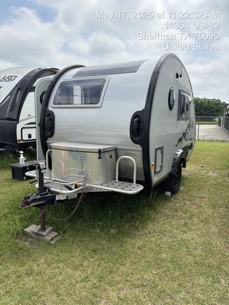 A modern silver teardrop RV, a great rv rental choice, featuring a front storage box, parked on green grass.