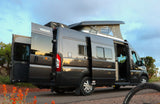 A gray Winnebago Solis camper van, great for RV rental and van life adventures, with open doors & pop-top extended at sunset.
