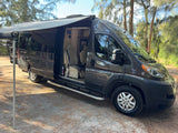 Dark gray Entegra Ethos camper van rv rental with an extended awning, parked in a pine forest. The side door is open, showing the interior.
