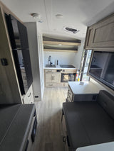 Bright modern RV rental interior featuring a kitchen with sink and microwave, plus dinette seating and a mounted TV.