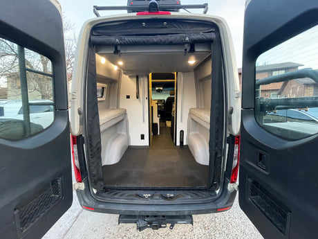 Rear view of this custom rv rental camper van, doors open to reveal its organized interior with sleeping platforms and storage.