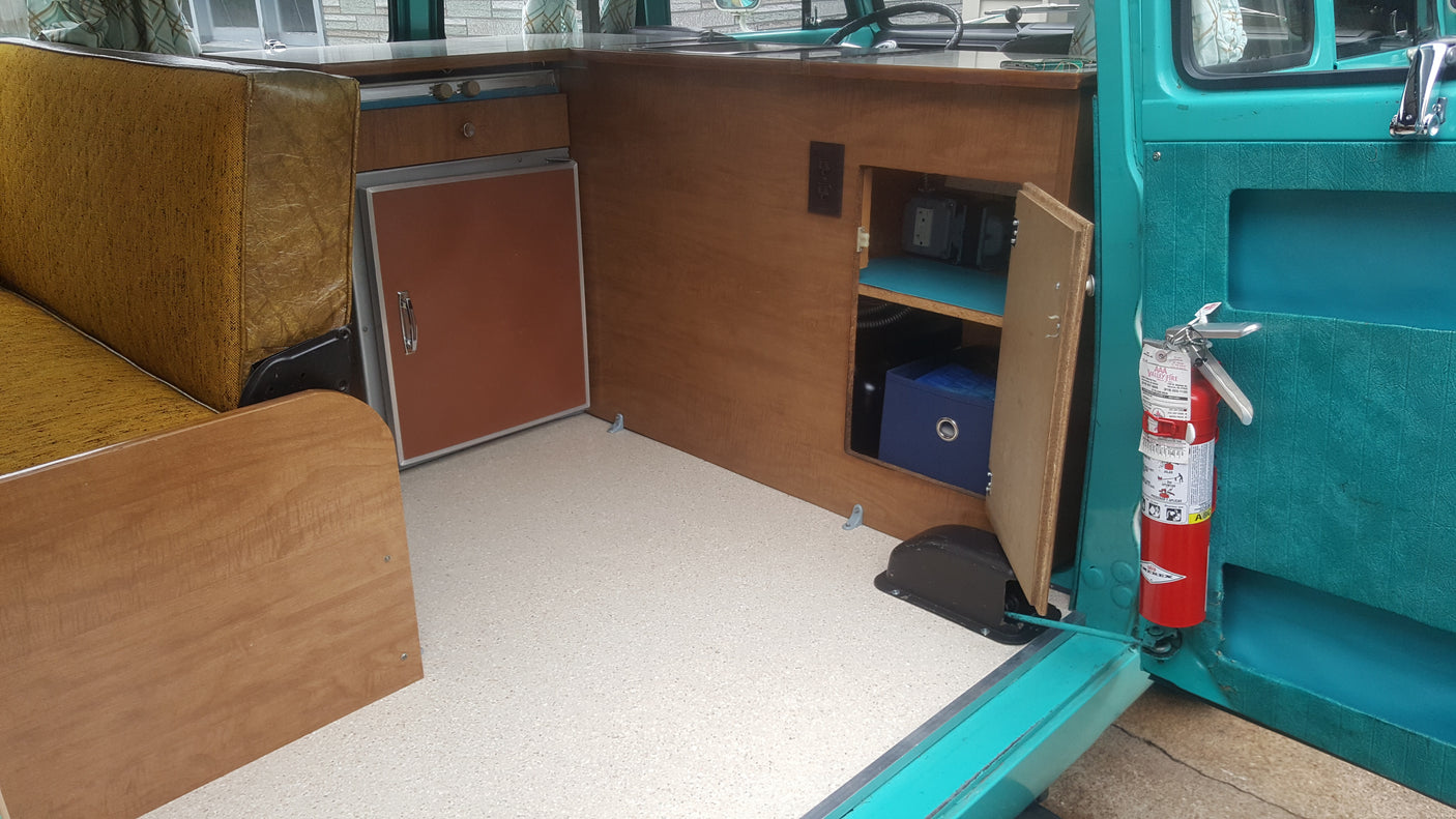 RV rental interior: A vintage camper setup with a mini-fridge, wood cabinetry, and a fire extinguisher for safety.