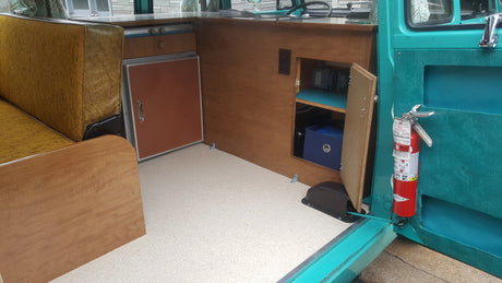 RV rental interior: A vintage camper setup with a mini-fridge, wood cabinetry, and a fire extinguisher for safety.