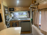 Inside this organized **rv rental** kitchen: compact sink, stove, fridge, labeled cabinets for plates/spices, and dining area.