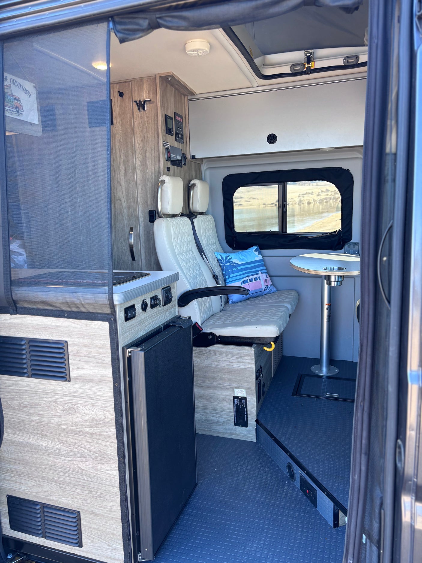 This rv rental features a cozy camper van interior: a compact dining area, kitchenette, plush seating, and scenic window views.