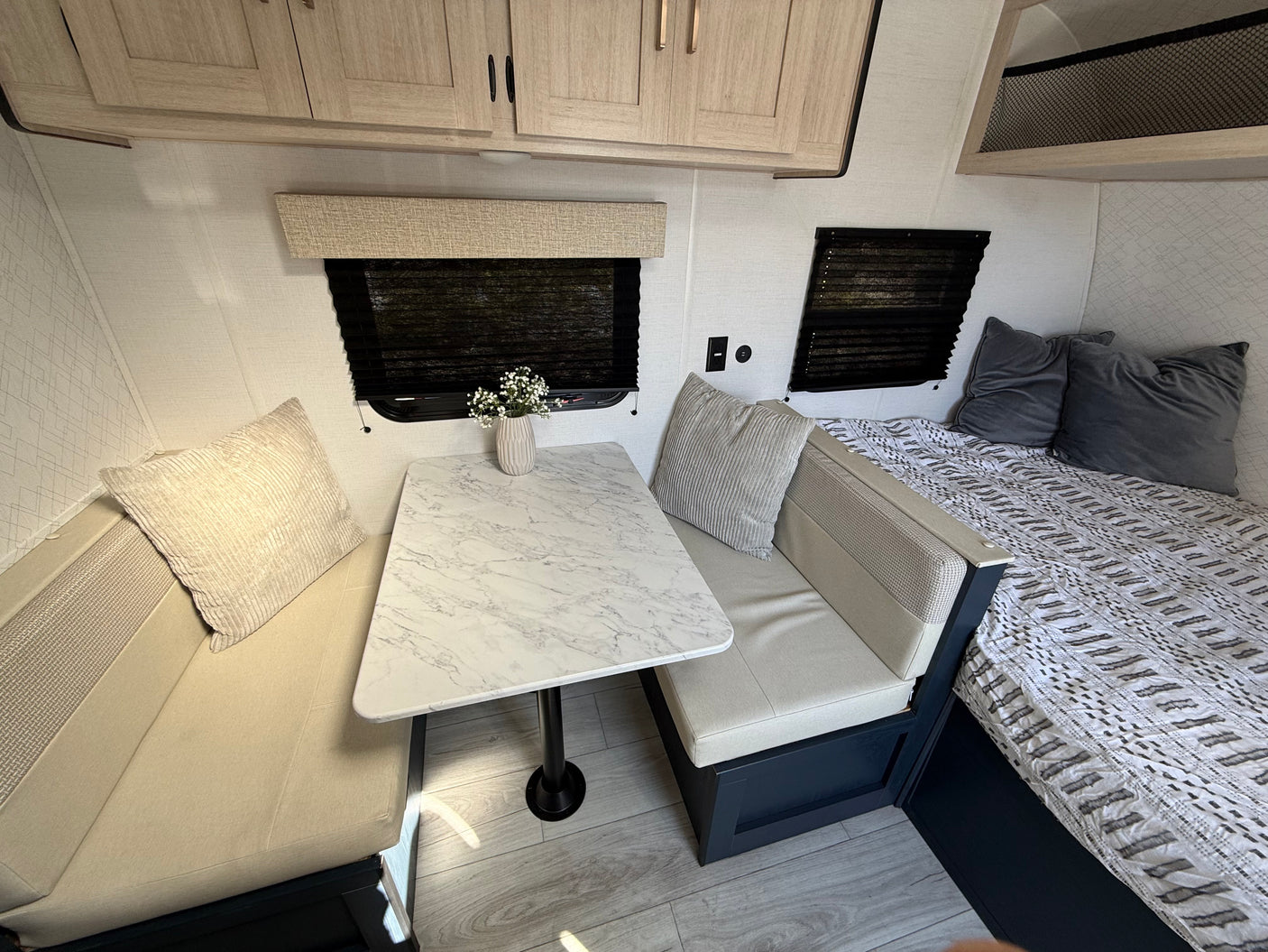 Stylish RV rental interior: dinette with marbled table, plush benches, and bed with patterned bedding, plus overhead cabinets.