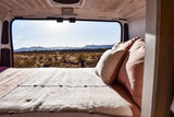 Cozy bed in an RV rental, offering stunning desert mountain views from the open back. Experience peaceful van life!