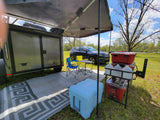 Cozy RV rental camp with an InTech trailer, awning, chairs, table, and cooler, creating an ideal outdoor living space.