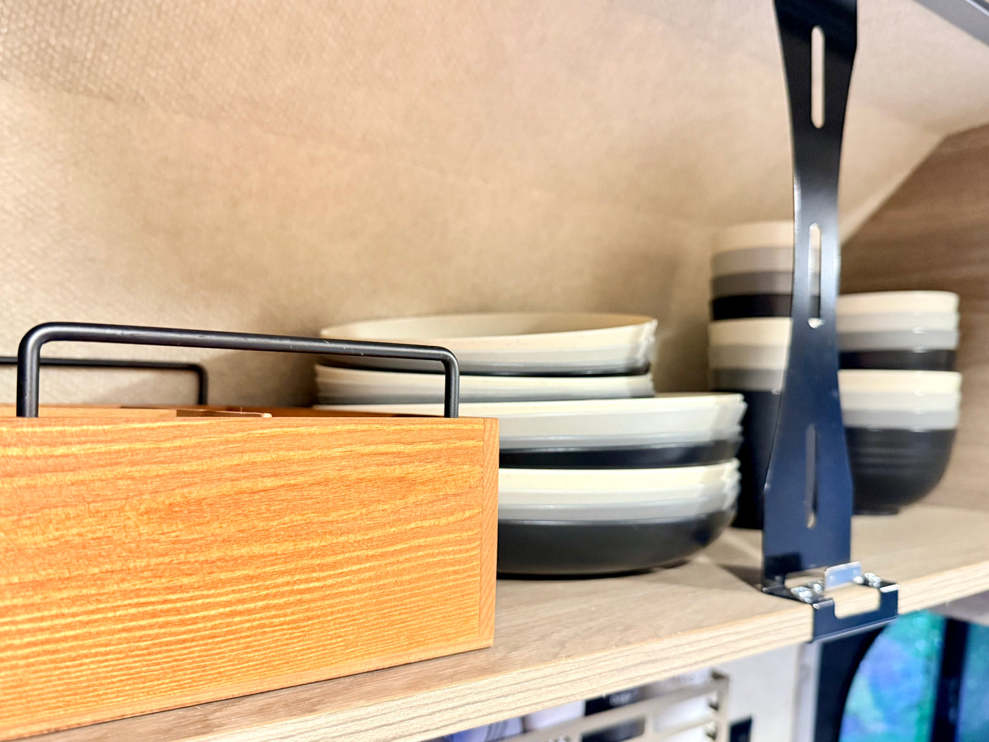 Organized RV rental kitchen with stacked plates & bowls in white, gray, and black, a wooden caddy, and metal shelf divider.