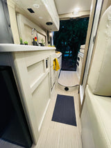 Modern RV rental interior: functional kitchen with light wood cabinets, sink, and outdoor scenery.