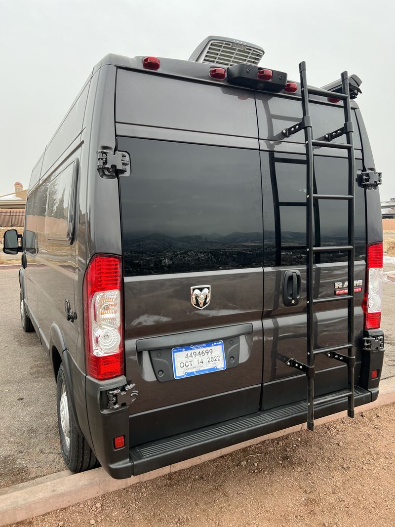  and|Inside an RV rental: a cozy bed above a pull-out storage tray. Wood accents & lighting create a modern mobile|Rear view of a dark gray Ram ProMaster camper van RV rental — photo 7