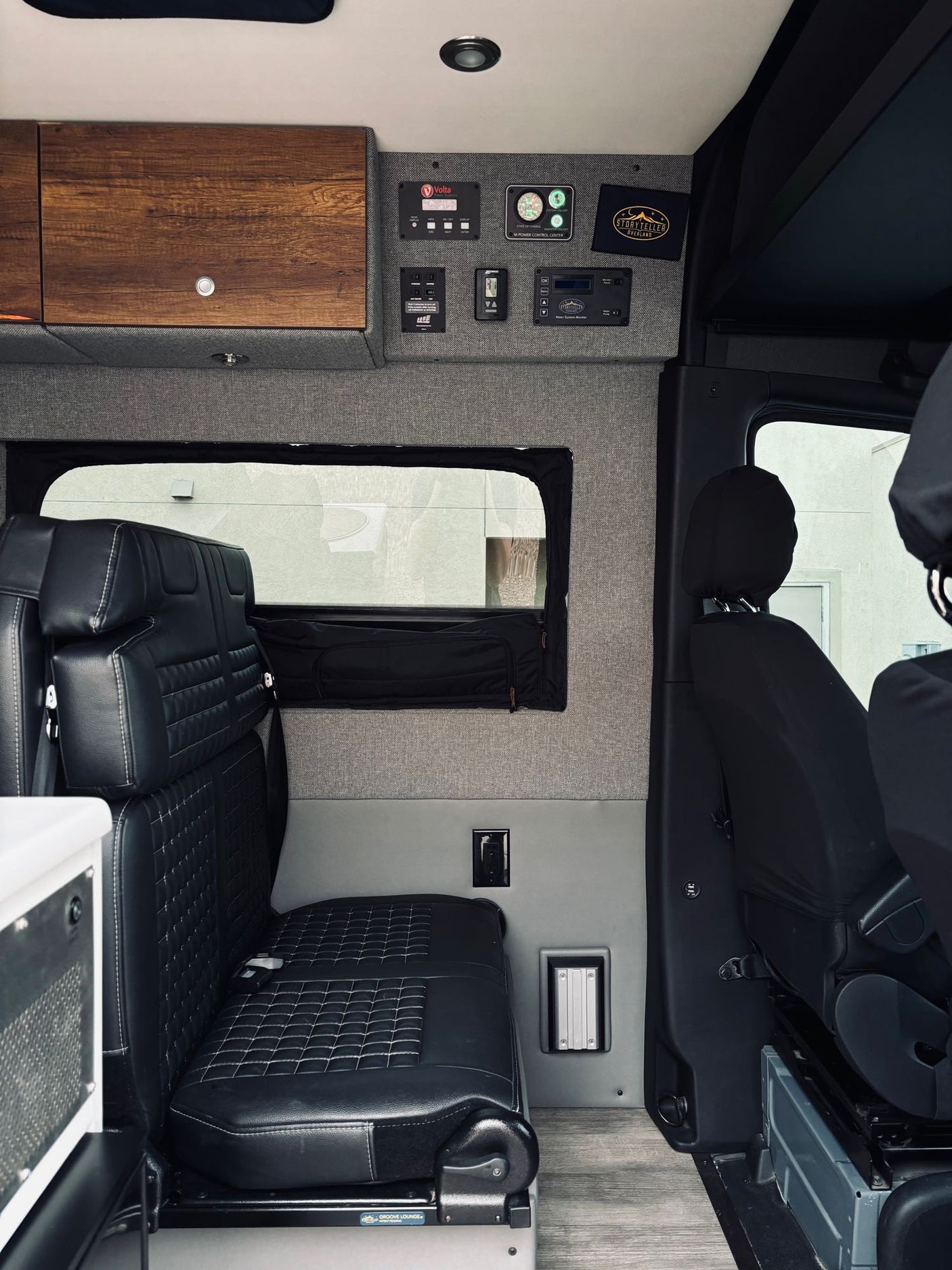 Interior of a modern camper van (RV rental) featuring plush black seating, smart control panels, and custom storage.