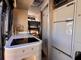 Compact rv rental interior with kitchenette (sink, cooktop), refrigerator, microwave, and bunk beds, plus a small bathroom.