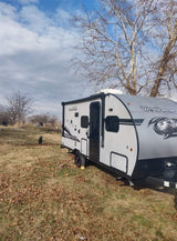 A modern Wolf Pup travel trailer, available for rv rental, is seen parked in a grassy field under a partly cloudy sky.