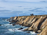 Explore the scenic coast! A lighthouse overlooks crashing waves and layered cliffs, an ideal stop for your RV rental adventure.