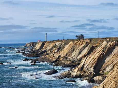 Explore the scenic coast! A lighthouse overlooks crashing waves and layered cliffs, an ideal stop for your RV rental adventure.