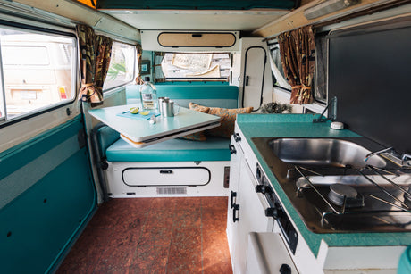 Explore this vibrant RV rental interior featuring a teal kitchenette, comfy bench seating, and a portable dining table setup.