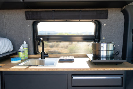 An RV rental's functional kitchen area: sink, black faucet, induction cooktop, and window views for your travels.