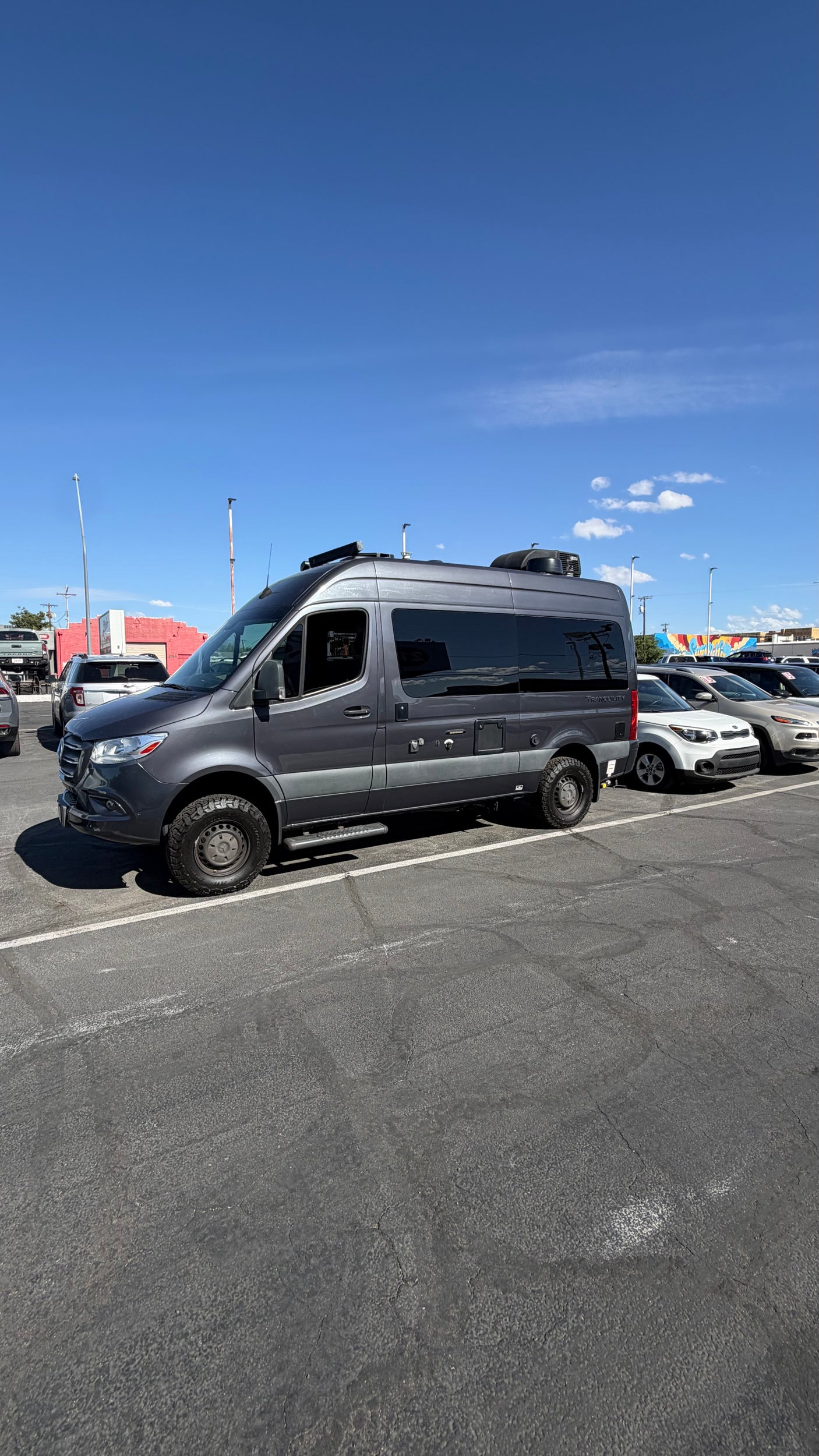 An adventure-ready grey Mercedes Sprinter rv rental, equipped with rugged tires, is parked outdoors under a blue sky.