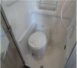 This compact RV rental bathroom includes a white toilet, shower head, and small wall-mounted shelf.