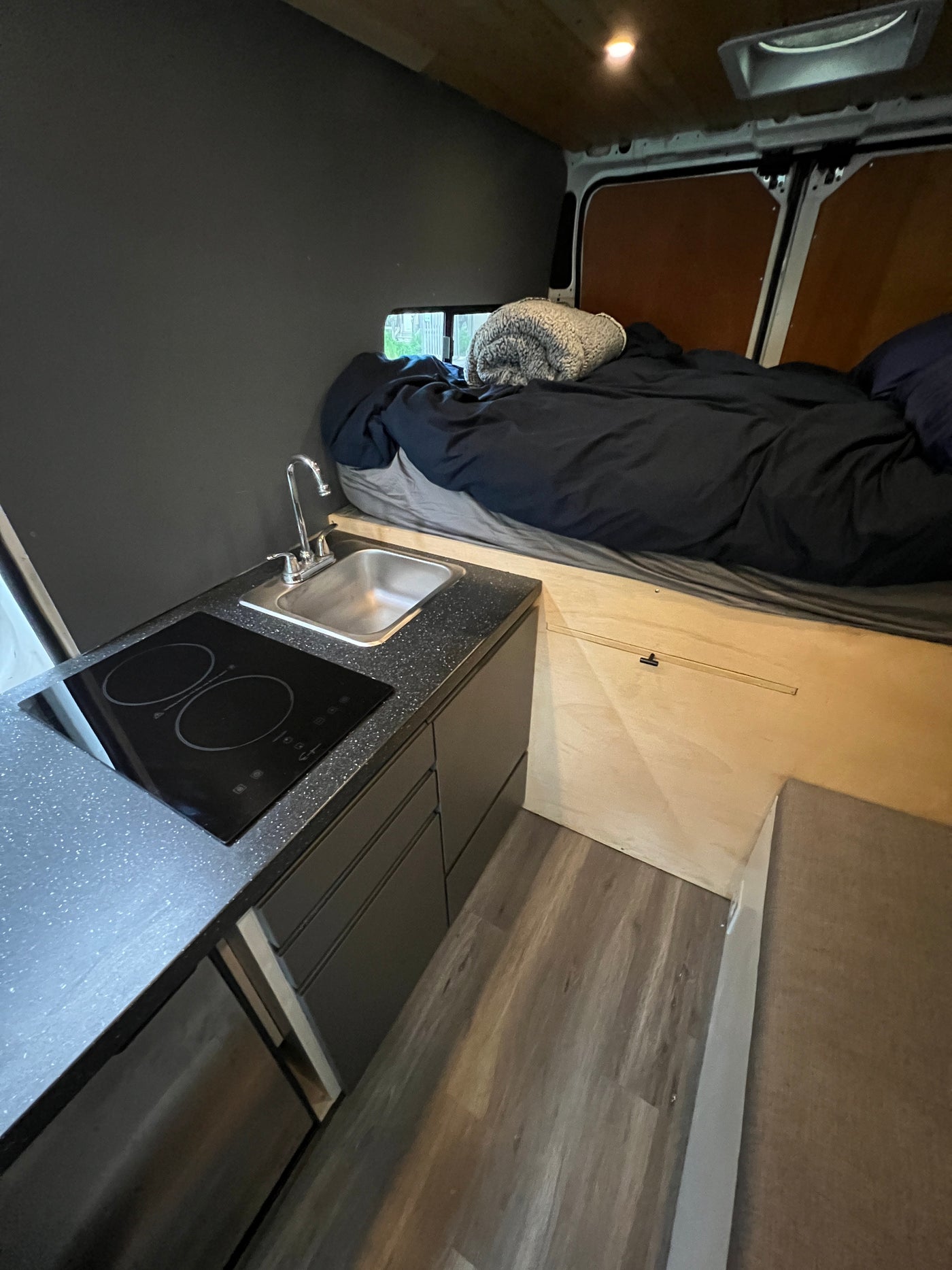 Compact & cozy RV rental interior: features a comfy bed, kitchen with sink & cooktop, and stylish storage solutions. — photo 3