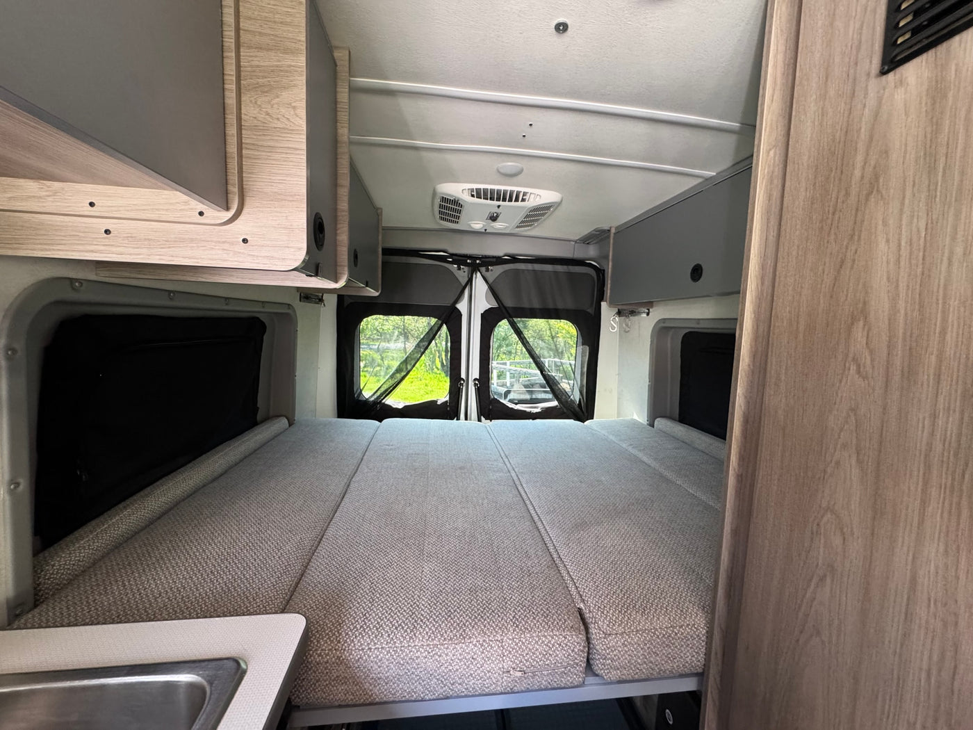 RV rental: Camper van interior shows a convertible bed, overhead storage, and nature views through open rear doors. — photo 9