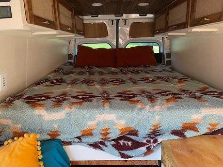 Spacious RV rental bedroom featuring a large bed with a patterned blanket and custom storage cabinets.