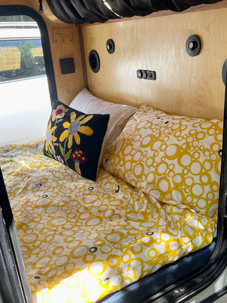 Inside this cozy rv rental, a bed with cheerful yellow and white patterned bedding, a floral pillow, and wood walls.