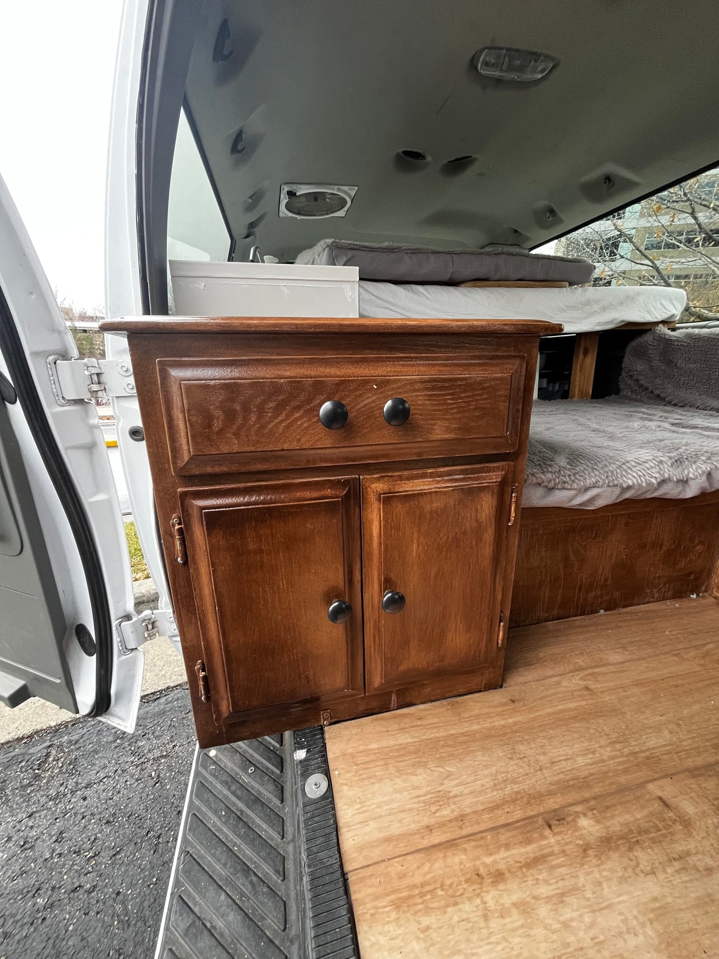 Inside this custom rv rental van conversion: a wood cabinet with storage, cozy bed, and durable wood flooring. — photo 12