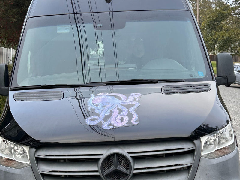  with a driver visible. Sunlight reflects off its dark tinted windows.|Black Mercedes Sprinter van RV rental features a vibrant octopus decal on its hood — photo 2