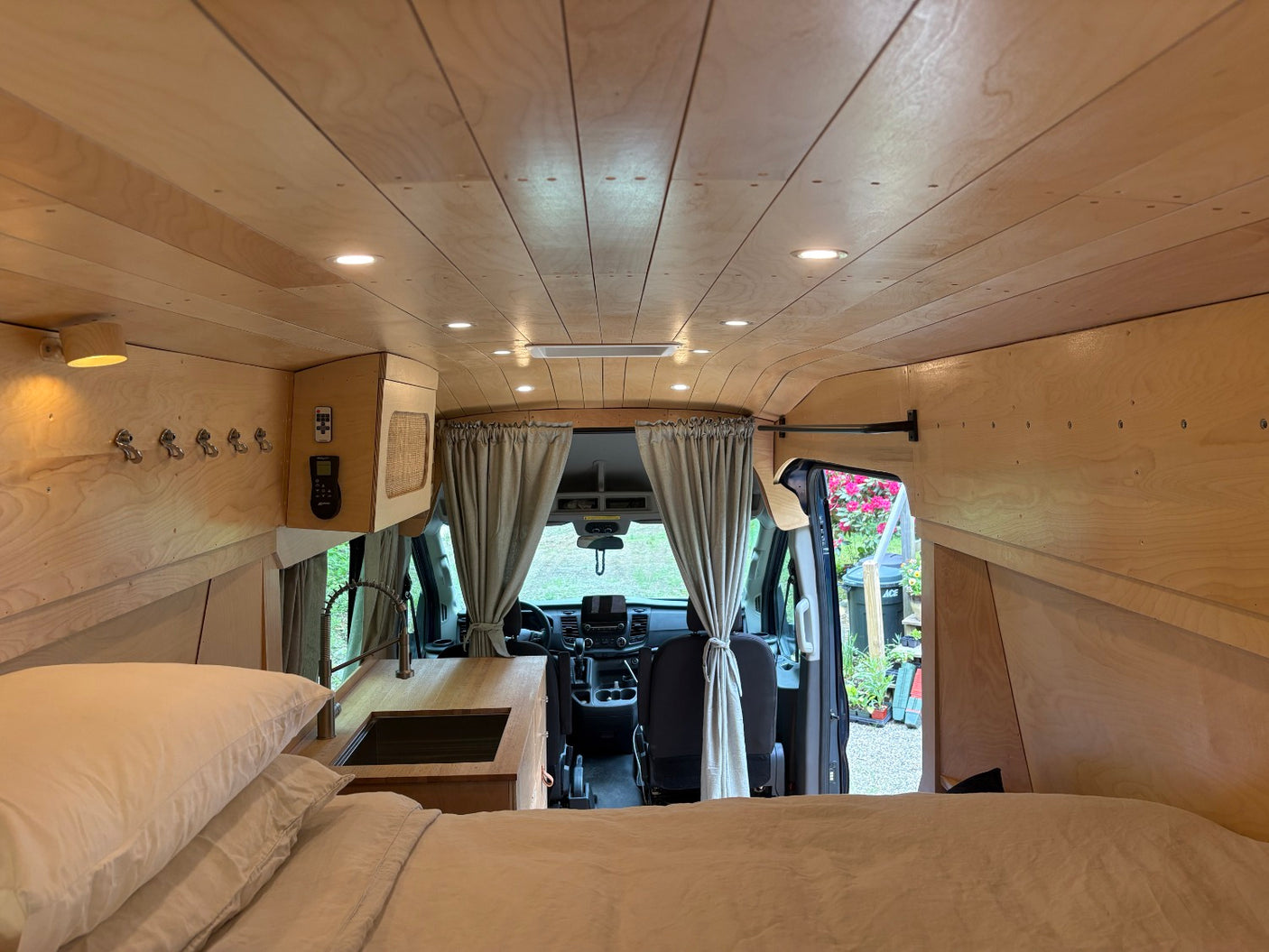 Inside this modern van conversion for rv rental: a cozy bed, sleek kitchen, and warm wood-paneled interior. Ready for adventure!