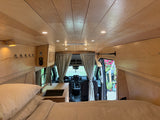 Inside this modern van conversion for rv rental: a cozy bed, sleek kitchen, and warm wood-paneled interior. Ready for adventure!